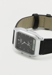 Quartzové hodinky Casio s pouzdrem ze stříbrné nerezové oceli, černým analogovým ciferníkem a digitálním displejem, doplněné černým koženým řemínkem.