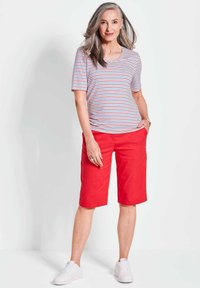 Gestreiftes kurzärmliges Hemd in Weiß, Rot und Blau; rote knielange Shorts; weiße Sneakers; glattes Material und lässige Passform.