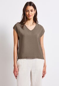 Blusa khaki a V in tessuto leggero, con maniche corte e vestibilità ampia, abbinata a pantaloni in lino chiari.