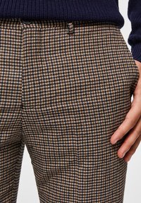 Bruna och beige houndstooth-mönstrade byxor med en strukturerad yta, rak snitt och framfickor. Bärs med en marinblå stickad tröja.