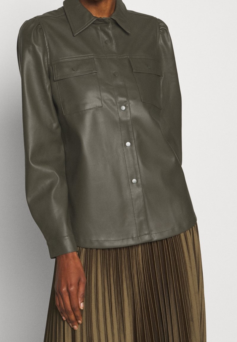 Veste chemise en cuir vert foncé avec deux poches avant, fermeture à boutons et un col. Texture lisse avec une coupe ajustée.