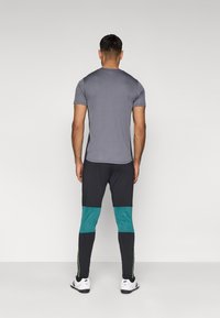 Ανδρικό αθλητικό σύνολο με εφαρμοστό γκρι κοντομάνικο μπλουζάκι και μαύρα κολάν με τιρκουάζ λεπτομέρειες και πράσινες ρίγες στα πλευρά.