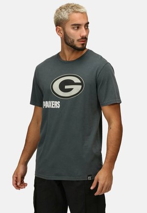 Camiseta de algodón gris con un logo circular prominente que presenta una "G" estilizada y el texto "PACKERS" debajo. Diseño clásico de cuello redondo.
