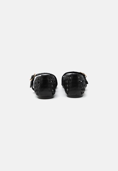 Paire de chaussures plates en cuir tressé noir avec brides à la cheville et boucles dorées, vues de dos sur fond blanc.