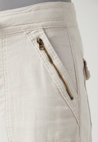 Beige bavlněné šortky s kapsou na zip a čistým provedením. Tkanina má hladkou strukturu s jemnými švy.