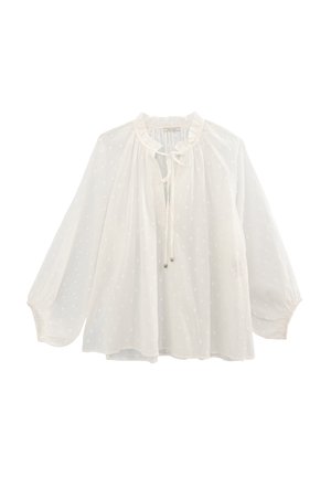 Blusa blanca de tela ligera, con un patrón de lunares, cuello con volantes, parte delantera ajustable con cordón y mangas largas y vaporosas.