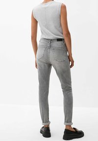 Šedý top bez rukávů, který je spárován se světle šedými skinny džíny s mírným pasem, ohrnutými manžetami a černými botami s dekorativními detaily.