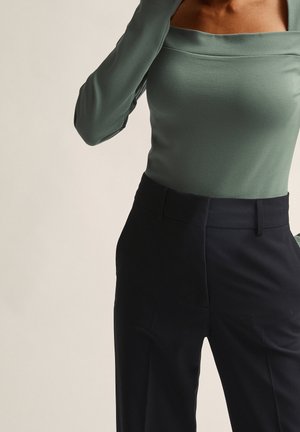 Green long-sleeve top with a square neckline and black high-waisted trousers. The materials are smooth with a fitted design.