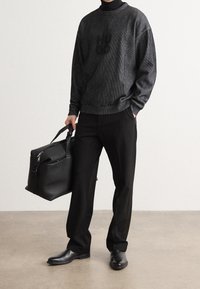 Sweat-shirt noir à texture côtelée avec logo, associé à un pantalon noir ample et des chaussures noires vernies, tenant un sac noir structuré.