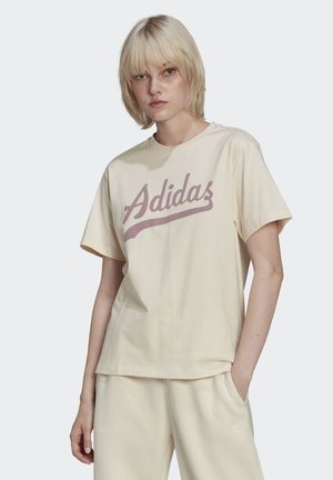 Krémové bavlnené tričko s veľkým ružovým logom "Adidas" v kurzívnom písme. Krátke rukávy a voľný strih s hladkým povrchom.