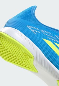 Talons de chaussure de sport bleue avec une semelle intermédiaire blanche et une semelle extérieure texturée jaune vif, comportant le logo de la marque et un détail en mesh sur le dessus.