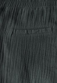 Dark green textured fabric featuring a wrinkled pattern, with an inset pocket on the right side. Elastic waistband for adjustable fit.