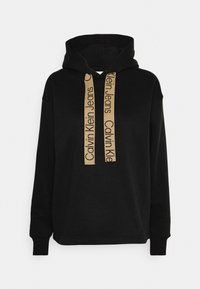 Czarna bluza z kapturem wykonana z miękkiego materiału, z dużą kieszenią kangurką i beżowymi sznurkami z nadrukiem "Calvin Klein Jeans" w kolorze czarnym.