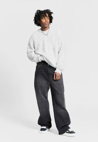 Light gray, fluffy sweater with wide sleeves, paired with loose-fitting, dark gray jeans and black and white sneakers. Simple design and textures.