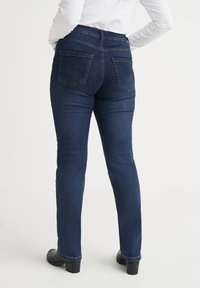 Högmidjade mörkblå jeans i denim med bakfickor, smala ben och en slät yta. Har en sydd midja och lätt stretch.