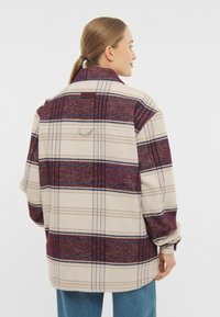 Jachetă din fleece de culoare crem cu un model de tartan în nuanțe de vișiniu și albastru, având guler și un finisaj texturat. Vederea din spate arată o croială lejeră și detalii de cusătură.