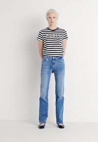Camiseta a rayas blanca y negra con el texto "PARÍS", combinada con jeans rectos de un azul claro y bailarinas negras. Estilo minimalista y casual.