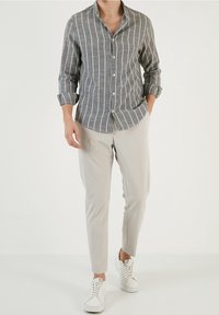 Grijs gestreept overhemd met een kraag, opgerolde mouwen, gecombineerd met lichtbeige slim-fit broeken en witte sneakers.