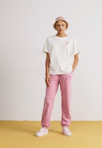 Afslappet hvid bomulds t-shirt med et rosa logo, parret med rosa joggerbukser. Hvide sneakers fuldender det afslappede outfit.