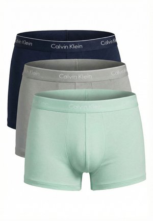 Trois boxers pour hommes en vert menthe, gris et bleu marine, chacun avec une ceinture portant la marque Calvin Klein.