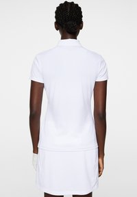 Vit polo med kort ärm och krage, kombinerad med en vit kjol. Slät tygtextur, minimalistisk design utan mönster.