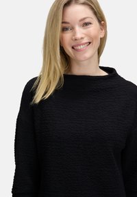 Schwarzer strukturierter Pullover mit weitem Ausschnitt und langen Ärmeln, der aus leicht zerknittertem Stoff besteht, um zusätzliches visuelles Interesse zu bieten.