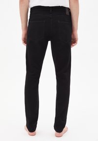 Pantalons en denim noir à coupe droite, avec deux poches arrière et une étiquette de marque visible sur la ceinture.