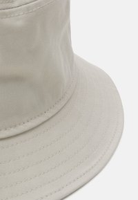 Lys beige bøttehat lavet af ribbet stof. Har en bred, flad skygge og subtile stikninger langs kanterne.