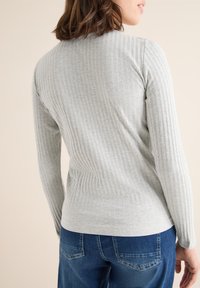 Světlé šedé žebrované tričko s dlouhým rukávem vyrobené z měkké látky, s přiléhavým střihem a kulatým výstřihem, spárované s modrými denimovými džínami.