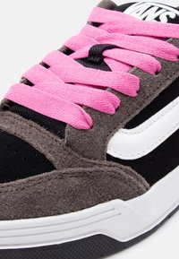 Κοντινό πλάνο σε αθλητικό παπούτσι με καφέ σουέτ, μαύρο ύφασμα, λευκό λογότυπο, λευκή σόλα και φωτεινά ροζ κορδόνια δεμένα σε τυπικό σταυρωτό μοτίβο.