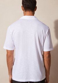 Witte polo met korte mouwen, voorzien van een klassieke kraag, textuurstof en een relaxed fit. De achterkant heeft minimale details en geen grafische elementen.
