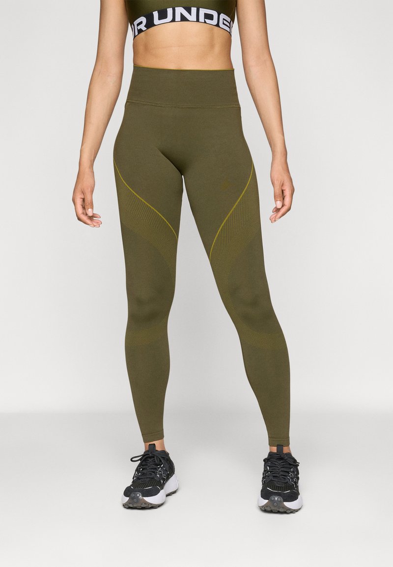 Magas derekú zöld leggings texturált oldalsó panelekkel és sárga díszítéssel, rugalmas anyagból készült, fekete sportcipővel párosítva.