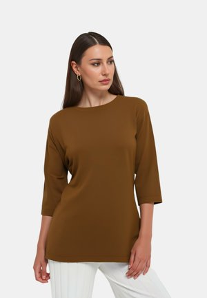 Maglia marrone a maniche lunghe con una vestibilità comoda e scollo tondo. Il tessuto liscio è abbinato a pantaloni bianchi a righe verticali.