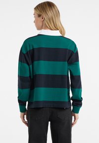 Polo a maniche lunghe con righe orizzontali blu navy e teal, colletto bianco e vestibilità rilassata. Realizzato in morbido cotone.
