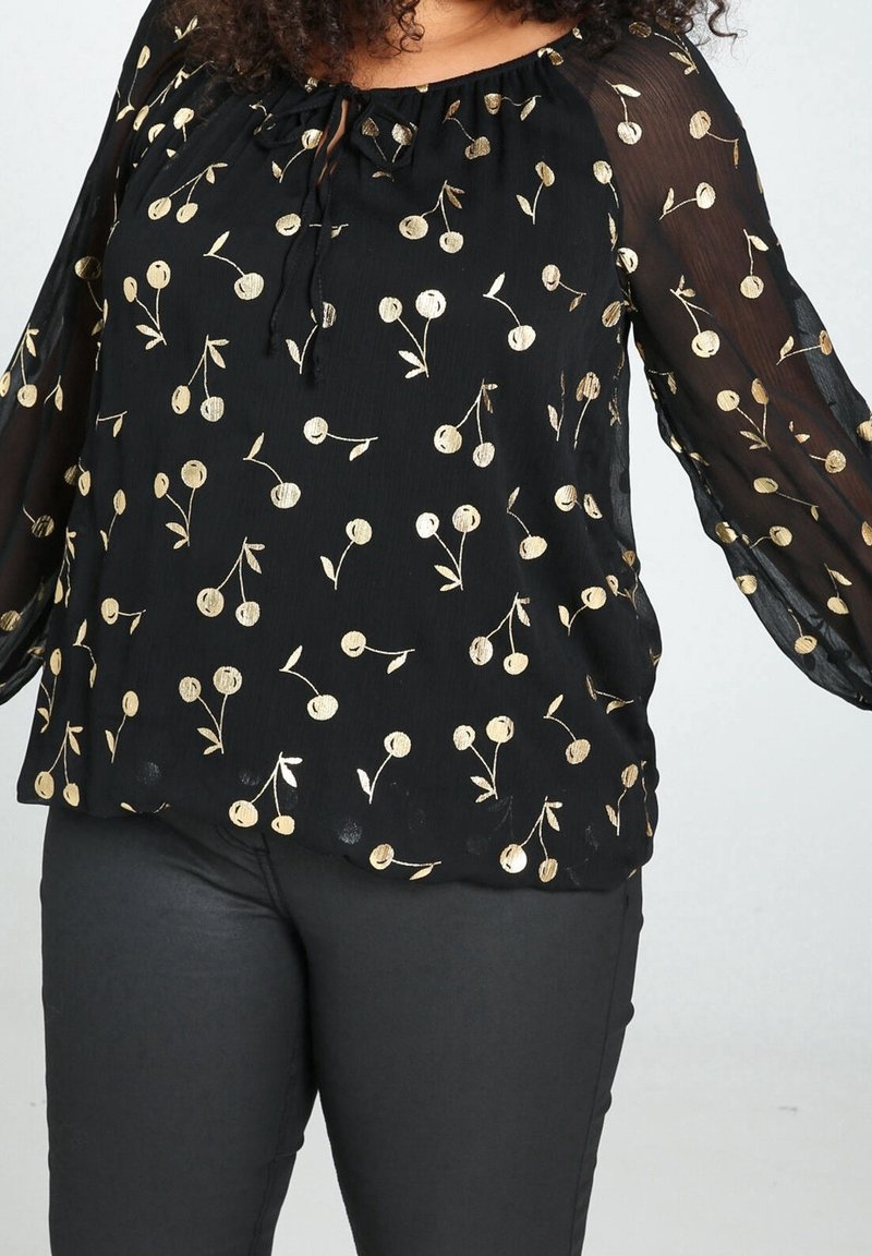 Blouse noire avec manches longues en voile transparent et col à cordon, ornée de motifs circulaires dorés et de petits dessins floraux.