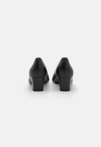 Czarne skórzane buty na słupku z gładką teksturą i zaokrąglonym noskiem. Posiadają niski obcas i minimalistyczny design bez zdobień.