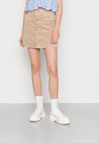 Saias mini de corduroy bege com fecho frontal em botão, apresentando bolsos e uma superfície texturizada, combinada com botas de combate brancas com atacadores.