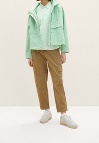 Mint green jacket with zip and button closure, striped shirt, beige cargo pants with pockets, and white sneakers with beige soles.