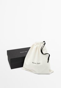 Sacchetto in cotone bianco con coulisse, lettering nero e scatola di cartone nera con la stessa grafica. Entrambi gli oggetti sono disposti ordinatamente.