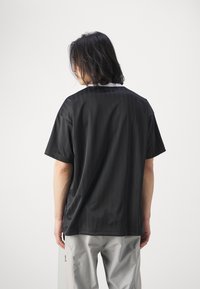 Musta lyhythihainen paita, jossa on tekstuuripinta, valkoisella kauluksella ja rento malli, nähtynä takaa.