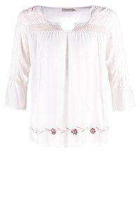 Blouse blanche avec manches trois-quarts, encolure smockée, détail en forme de trou et broderie florale le long de l'ourlet.
