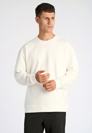 Witte sweatshirt met een ronde hals, verlaagde schouders en geribbelde boorden. Zachte textuur, minimalistisch ontwerp, gecombineerd met zwarte broek.