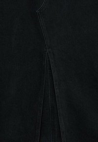 Tissu en denim noir affichant une fente verticale avec une couture renforcée en haut de la fente.