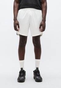 Λευκό αθλητικό παντελόνι σόρτς με άνετη εφαρμογή, σε συνδυασμό με μαύρα αθλητικά παπούτσια και λευκές κάλτσες. Σύντομο σχέδιο, απαλό ύφασμα και ελαστική μέση.