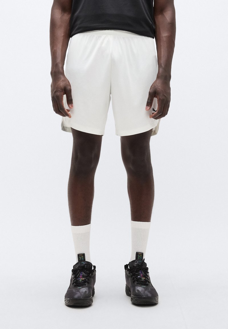 Λευκό αθλητικό παντελόνι σόρτς με άνετη εφαρμογή, σε συνδυασμό με μαύρα αθλητικά παπούτσια και λευκές κάλτσες. Σύντομο σχέδιο, απαλό ύφασμα και ελαστική μέση.