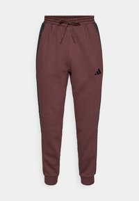 Tum�ši sarkanas sporta bikses ar melniem sānu paneļiem, elastīgu jostasvietu un regulējamu auklu. Uz kreisā apakšējā kājas ir Adidas logo.