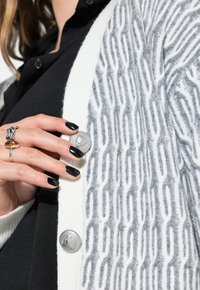 Cardigan grigio e bianco con motivo a disegno, caratterizzato da una trama testurizzata, bottone argentato e una camicia nera a strati sotto.