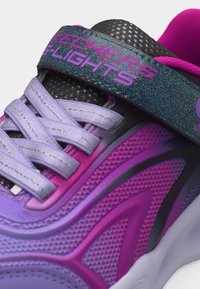 Κοντινή φωτογραφία sneaker Skechers σε μωβ και ροζ χρώμα, με λουράκι που φωτίζει και άσπρα κορδόνια, σε λευκό φόντο.