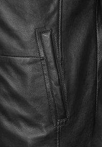 Zwart leren jack close-up, met een gladde textuur, opvallende stiksels en een zijzak met een slank ontwerp.