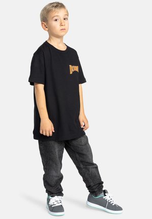 Zwarte katoenen T-shirt met oranje logo, gecombineerd met donkere denim jeans. Grijze sneakers met lichtblauwe accenten en witte veters.